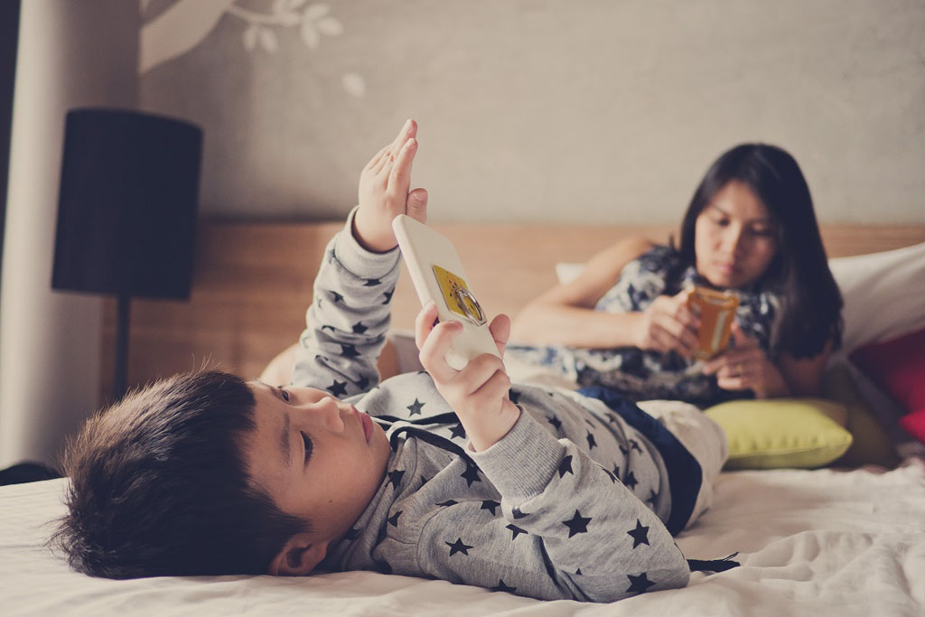 Asian chinese children playing tablet with mother on bed (Shutterstock)